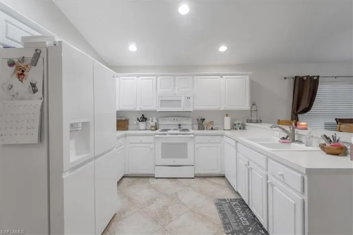 Kitchen with white cabinets, kitchen peninsula, white appliances, and light tile patterned floors