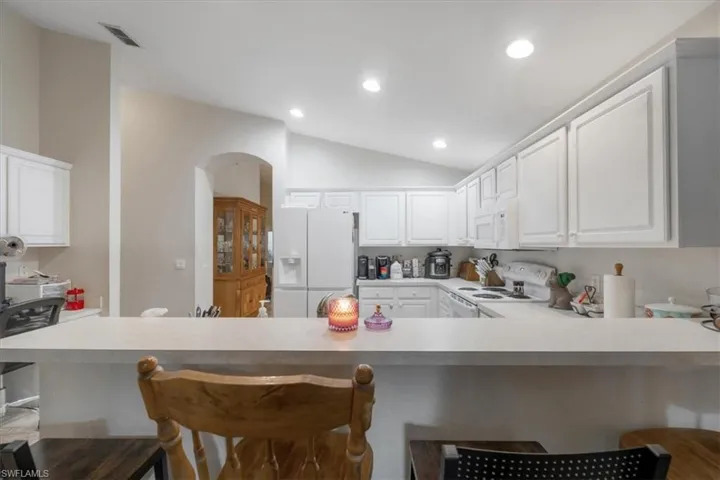 Kitchen with white appliances, kitchen peninsula, white cabinets, vaulted ceiling, and a kitchen bar