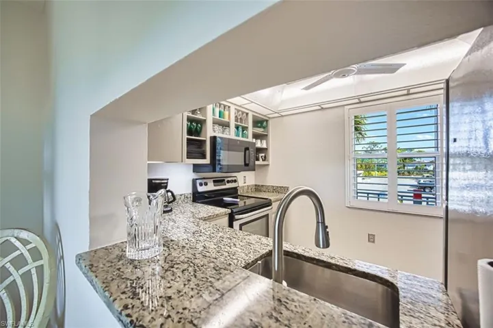 Kitchen with stainless steel appliances, light stone counters, ceiling fan, and open shelves