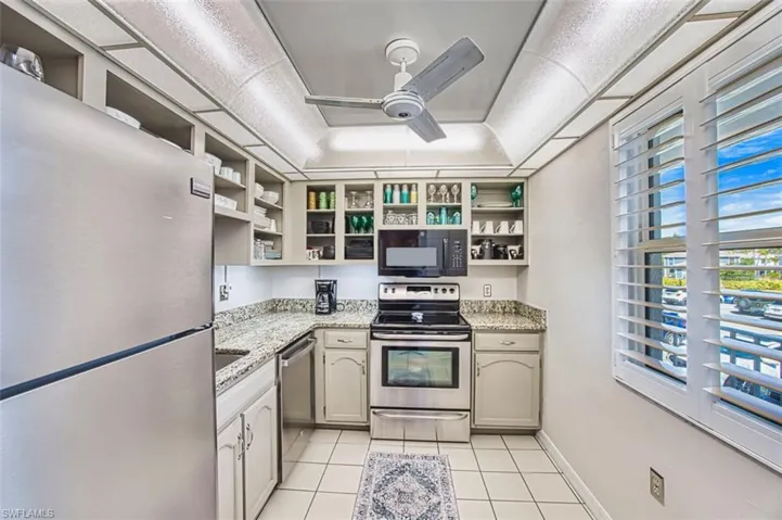 Kitchen with appliances with stainless steel finishes, ceiling fan, light stone countertops, and light tile patterned floors