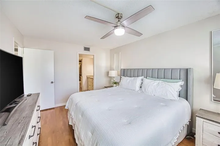 Bedroom featuring light wood finished floors, a ceiling fan, ensuite bathroom, and a textured ceiling