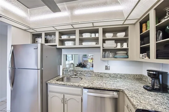 Kitchen with appliances with stainless steel finishes, light stone counters, open shelves, and white cabinets