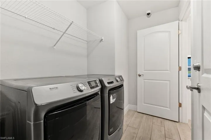 Dedicated laundry area featuring wood-finish flooring, light gray walls, and a white wire shelving unit for storage