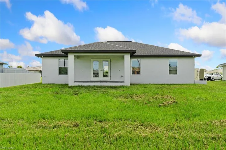 Rear exterior featuring a covered patio, double French doors, multiple windows, and a fenced perimeter
