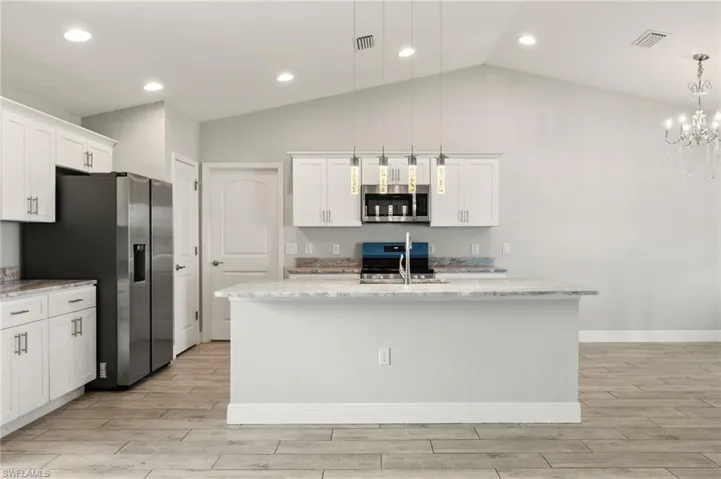 Kitchen featuring a central island with a sink, white cabinetry, integrated stainless steel appliances, and wood-finish flooring