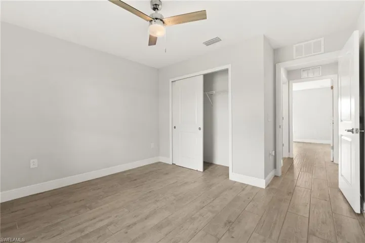 Bedroom featuring wood-finish flooring, a ceiling fan with integrated lighting, a sliding closet door, and crisp white baseboards
