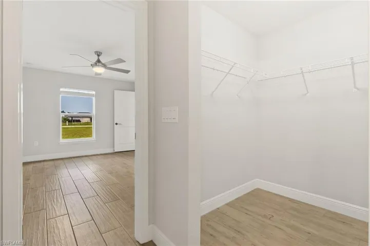 Bedroom featuring a ceiling fan with integrated lighting, wood-finish flooring, and a window overlooking a green expanse
