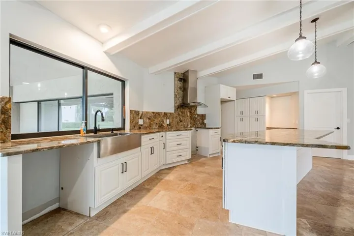 Kitchen featuring white cabinetry, lofted ceiling with beams, decorative light fixtures, and wall chimney range hood