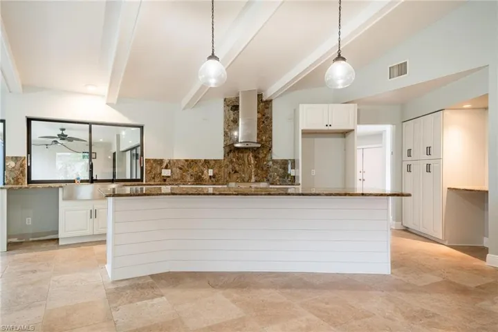 Kitchen with dark stone countertops, white cabinetry, wall chimney range hood, and tasteful backsplash