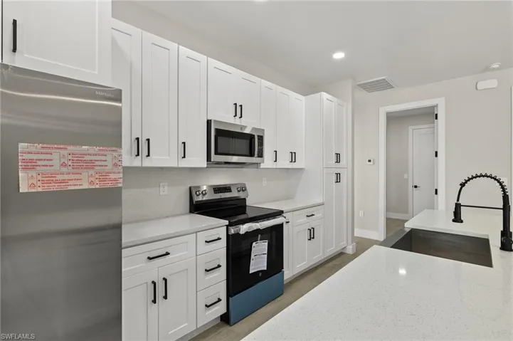 Kitchen featuring stainless steel appliances, light stone counters, sink, white cabinets, and light hardwood / wood-style floors