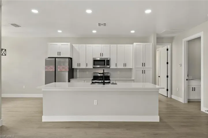 Kitchen featuring a center island with sink, light hardwood / wood-style flooring, appliances with stainless steel finishes, and white cabinetry