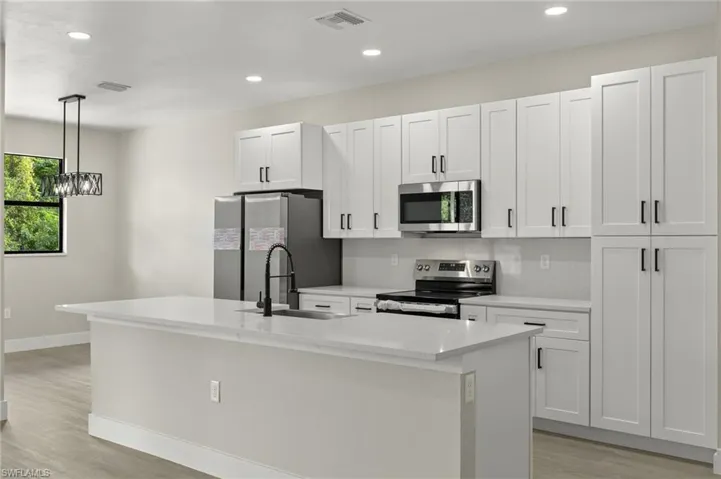 Kitchen with white cabinets, hanging light fixtures, appliances with stainless steel finishes, sink, and a center island with sink