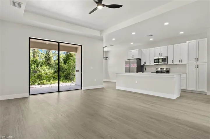 Kitchen with decorative light fixtures, light hardwood / wood-style flooring, appliances with stainless steel finishes, an island with sink, and ceiling fan