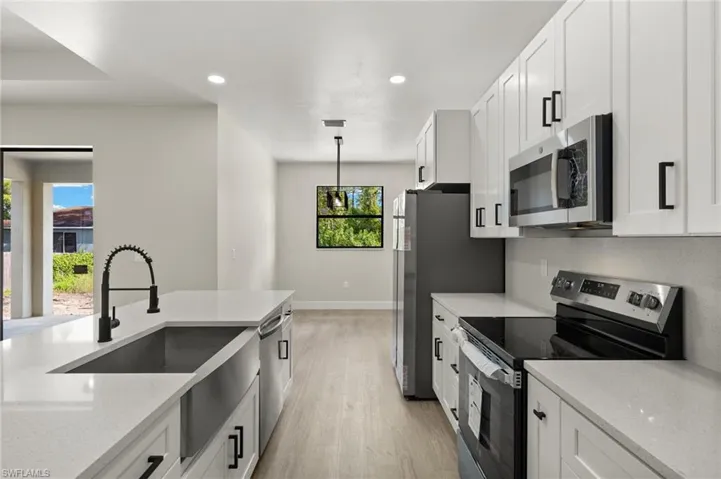 Kitchen with light stone counters, stainless steel appliances, white cabinetry, and light hardwood / wood-style flooring