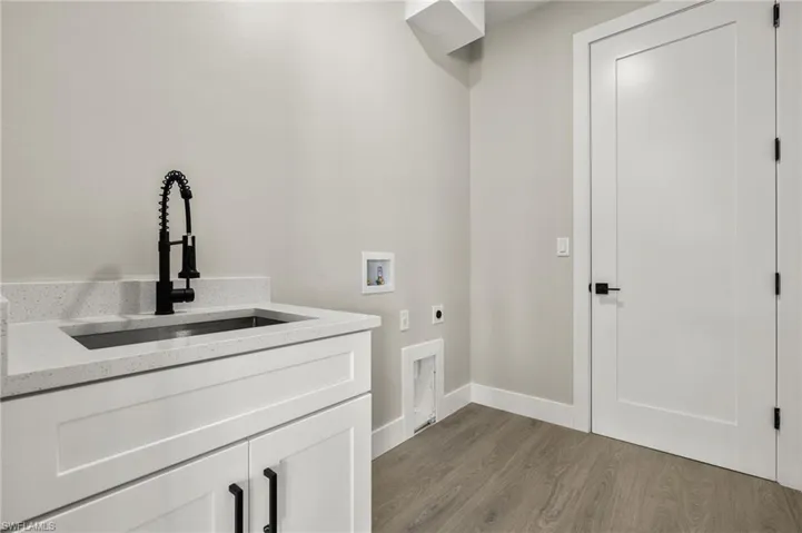Laundry room with light wood-type flooring, hookup for an electric dryer, sink, washer hookup, and cabinets