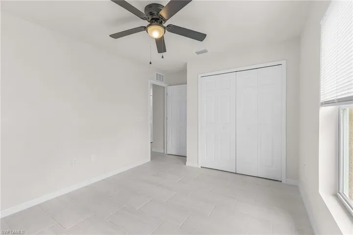 Unfurnished bedroom featuring a closet, light tile patterned floors, and ceiling fan