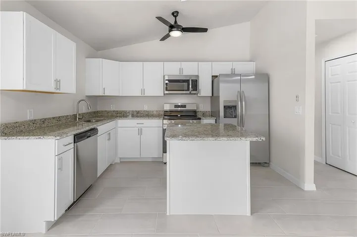 Kitchen featuring light tile patterned floors, a center island, ceiling fan, appliances with stainless steel finishes, and vaulted ceiling