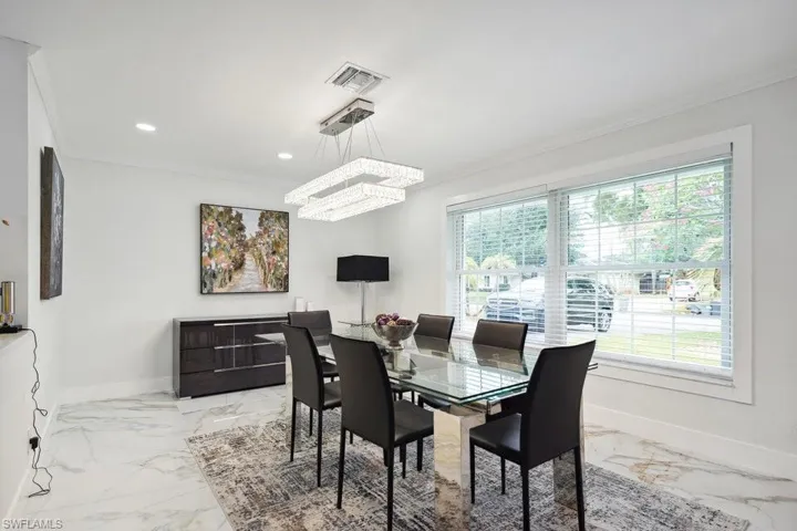Dining room with light marble finish flooring, ornamental molding, a chandelier, healthy amount of natural light, and recessed lighting