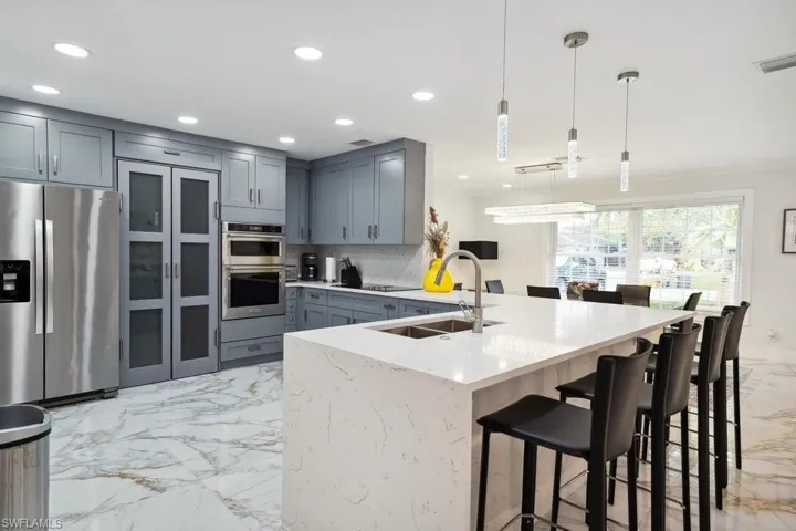 Kitchen with light marble finish floors, appliances with stainless steel finishes, backsplash, a breakfast bar area, and recessed lighting