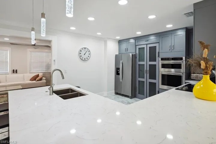 Kitchen featuring light stone counters, appliances with stainless steel finishes, hanging light fixtures, recessed lighting, and glass insert cabinets