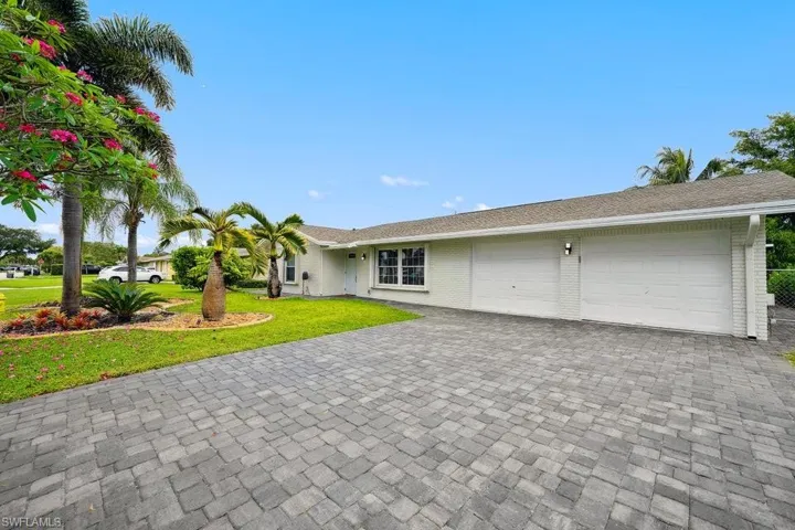 Ranch-style house featuring an attached garage, decorative driveway, brick siding, and a front lawn