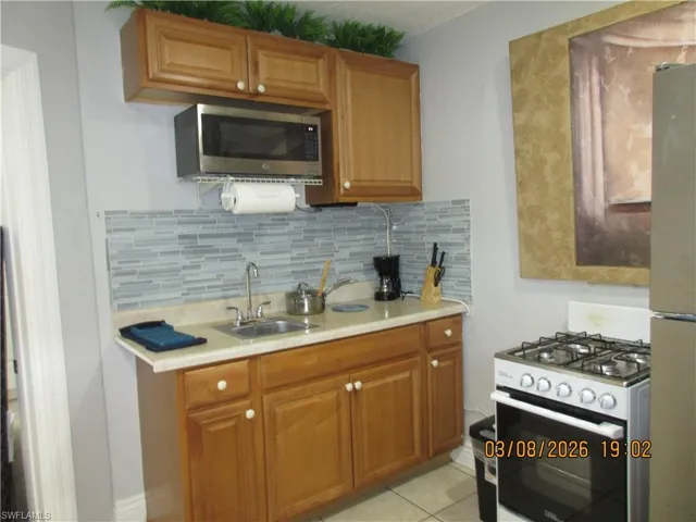 Kitchen featuring range with gas cooktop, light countertops, stainless steel microwave, freestanding refrigerator, and wood finish cabinetry