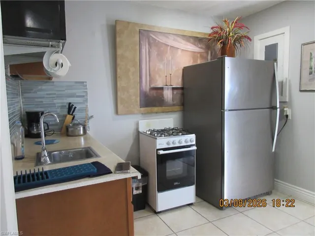 Kitchen featuring white range with gas stovetop, backsplash, light countertops, freestanding refrigerator, and light tile patterned floors