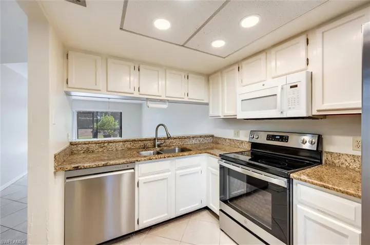 Kitchen featuring stainless steel appliances, light tile patterned flooring, white cabinetry, light stone counters, and recessed lighting