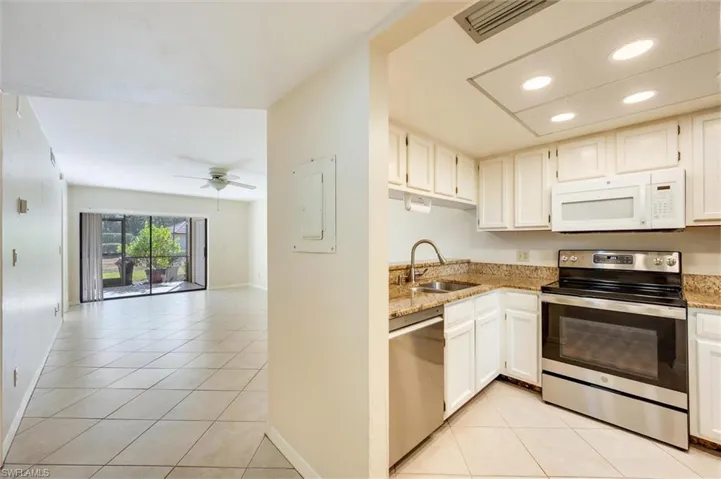 Kitchen with stainless steel appliances, light tile patterned floors, light stone countertops, recessed lighting, and white cabinetry