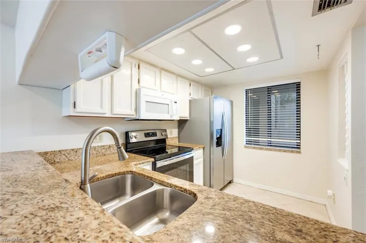 Kitchen featuring white cabinets, stainless steel appliances, recessed lighting, light stone countertops, and light tile patterned floors
