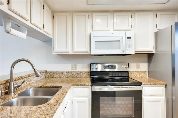 Kitchen with stainless steel appliances, white cabinets, and light stone counters