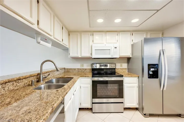 Kitchen featuring stainless steel appliances, light stone countertops, white cabinetry, and light tile patterned flooring