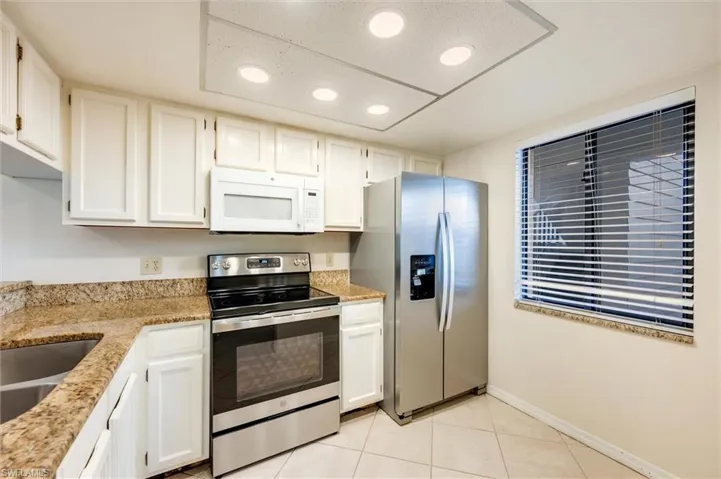 Kitchen featuring stainless steel appliances, light stone countertops, white cabinets, light tile patterned floors, and recessed lighting