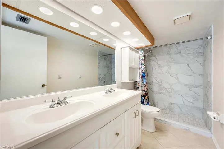 Full bathroom featuring double vanity, a marble finish shower, and recessed lighting