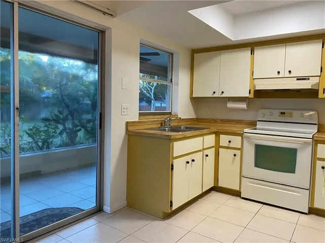 Kitchen featuring white electric range, light countertops, two tone cabinetry, and light tile patterned floors
