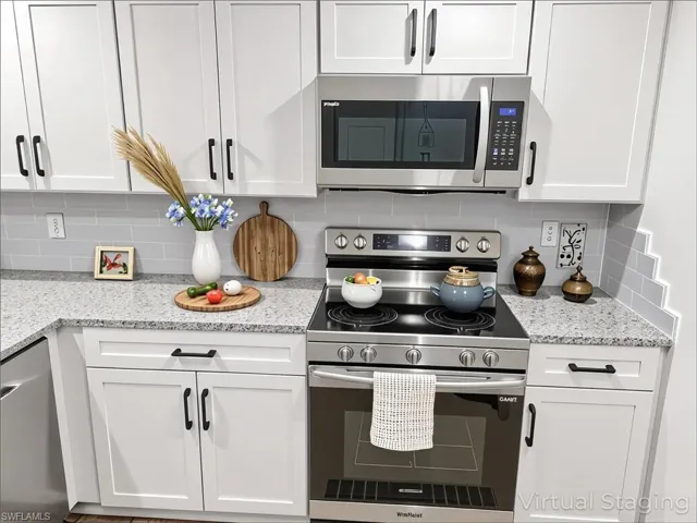 Kitchen with appliances with stainless steel finishes, white cabinetry, tasteful backsplash, and light stone counters