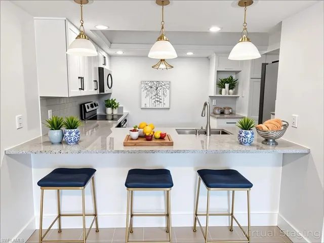 Kitchen featuring a peninsula, a kitchen bar, light stone countertops, appliances with stainless steel finishes, and recessed lighting