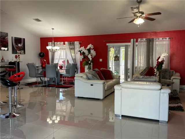 Unfurnished living room featuring visible vents, lofted ceiling, and ceiling fan with notable chandelier