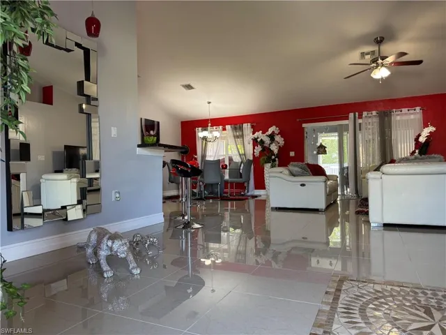 Living area featuring lofted ceiling, ceiling fan with notable chandelier, baseboards, and visible vents