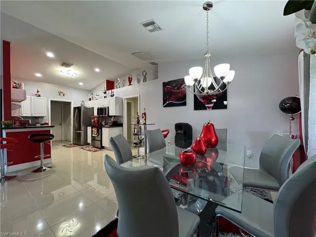 Dining room with visible vents, lofted ceiling, recessed lighting, light tile patterned flooring, and a notable chandelier
