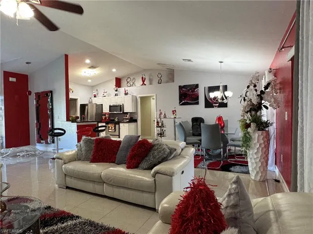 Living area featuring visible vents, ceiling fan with notable chandelier, light tile patterned flooring, and vaulted ceiling