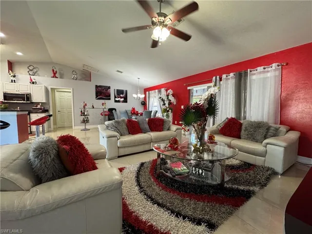 Living area with light tile patterned floors, visible vents, ceiling fan, and vaulted ceiling