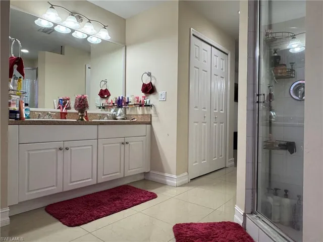 Bathroom with baseboards, double vanity, a stall shower, tile patterned floors, and a sink