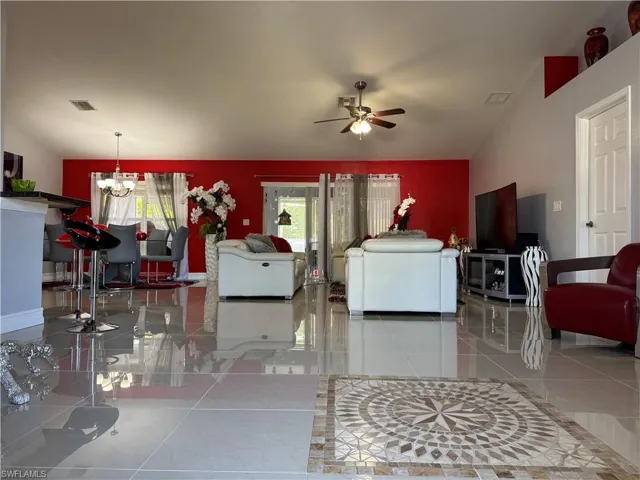 Living room featuring visible vents, ceiling fan with notable chandelier, and baseboards