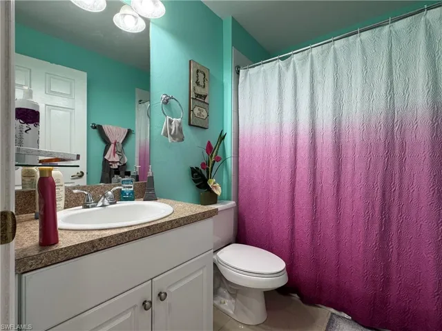 Bathroom with tile patterned floors, curtained shower, toilet, and vanity