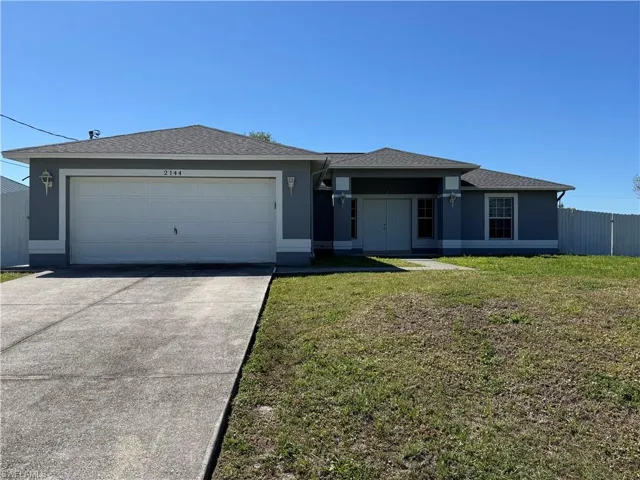 View of front of property with fence, driveway, stucco siding, a front lawn, and a garage