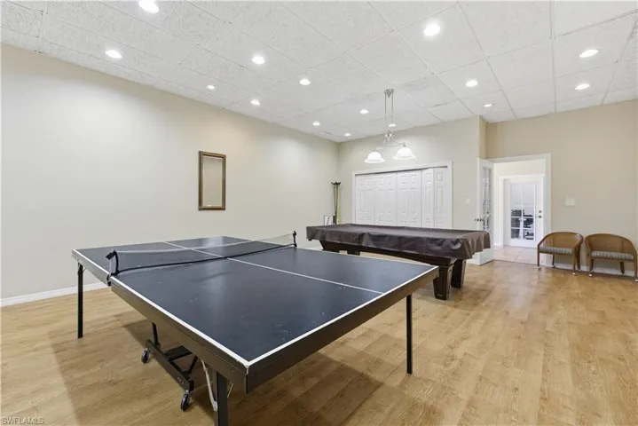 Spacious recreational room featuring wood-finish flooring, a drop ceiling with recessed lighting, and a pendant light fixture