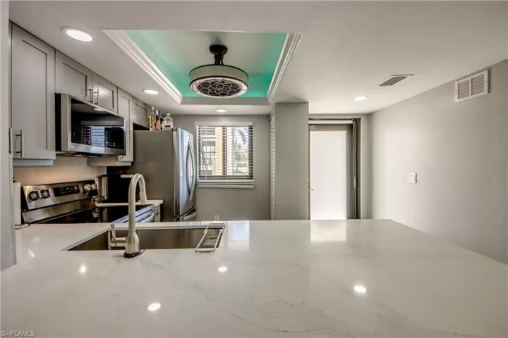Kitchen with stainless steel appliances, a tray ceiling, light stone countertops, gray cabinetry, and backsplash
