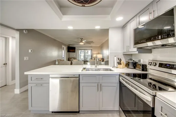 Kitchen with stainless steel appliances, gray cabinetry, a peninsula, open floor plan, and ornamental molding