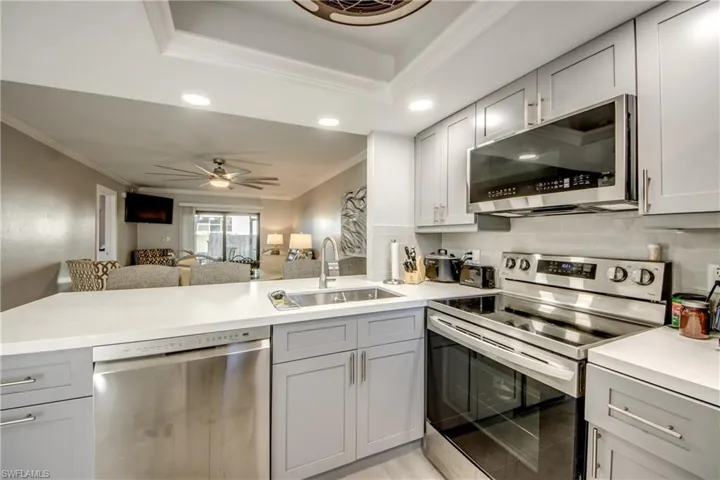 Kitchen with appliances with stainless steel finishes, gray cabinets, crown molding, open floor plan, and a peninsula
